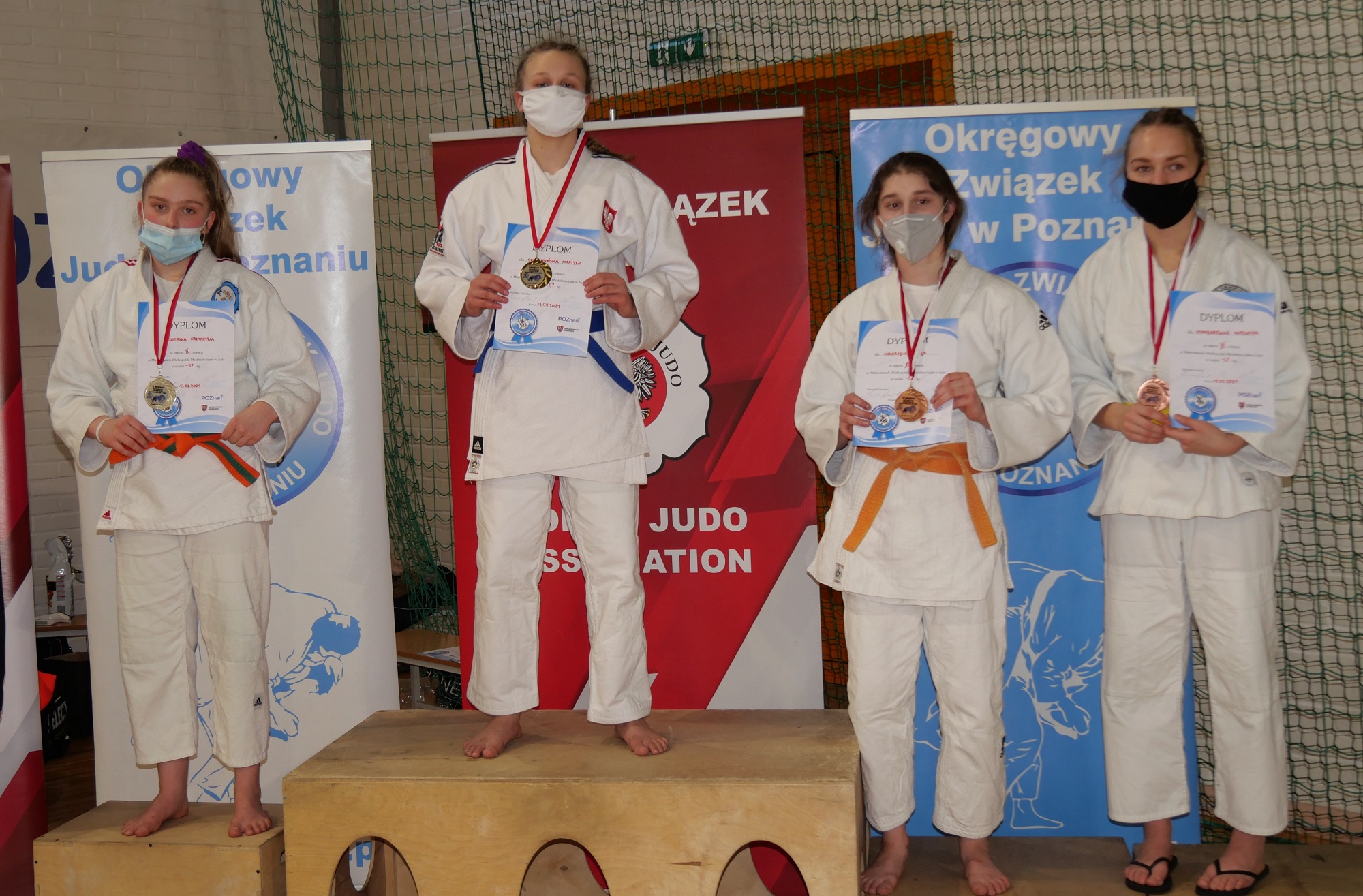Cztery zawodniczki judo na podium. W strojach sportowych i maseczkach ochronnych.