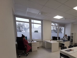 zdjęcie biura, dwie kobiety siedzą przy biurkach,które znajdują się pod oknami.