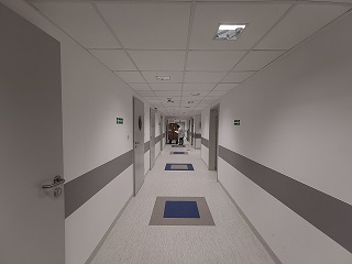 zdjęcie korytarza, długa perspektywa, po prawej i po lewej stronie szare drzwi. ściany białe
