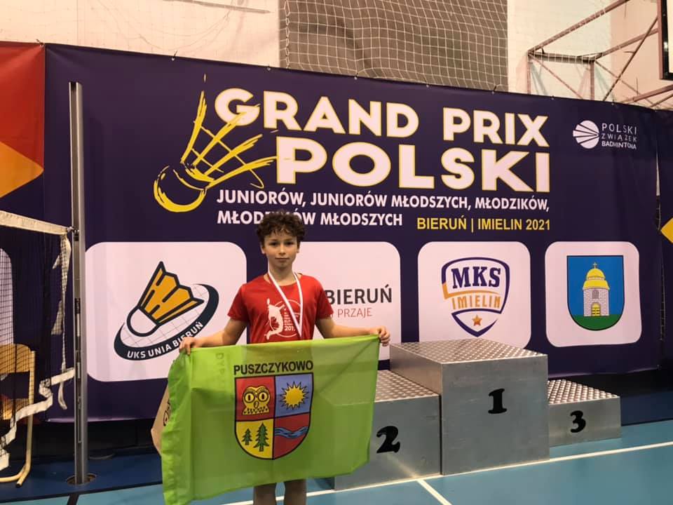 Chłopiec z zieloną flagą Puszczykowa na tle granatowego baneru z napisem Grand Prix Polski Juniorów.